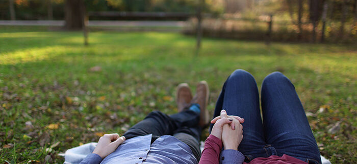 A couple holding hands and laying on the grass in a park