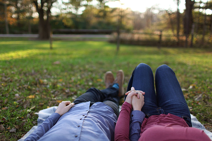 A couple holding hands and laying on the grass in a park