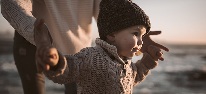 A person holding the hands of a young child as they walk.