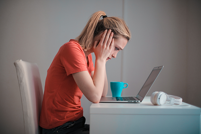 A woman looking stressed hunched over a laptop.