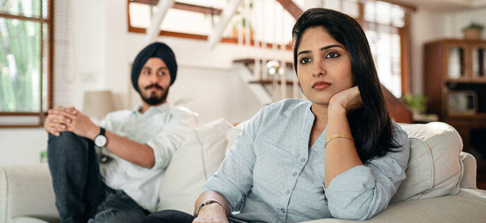 A couple sitting on a couch looking sad.