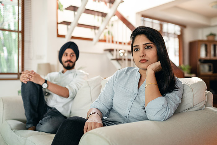 A couple sitting on a couch looking sad.